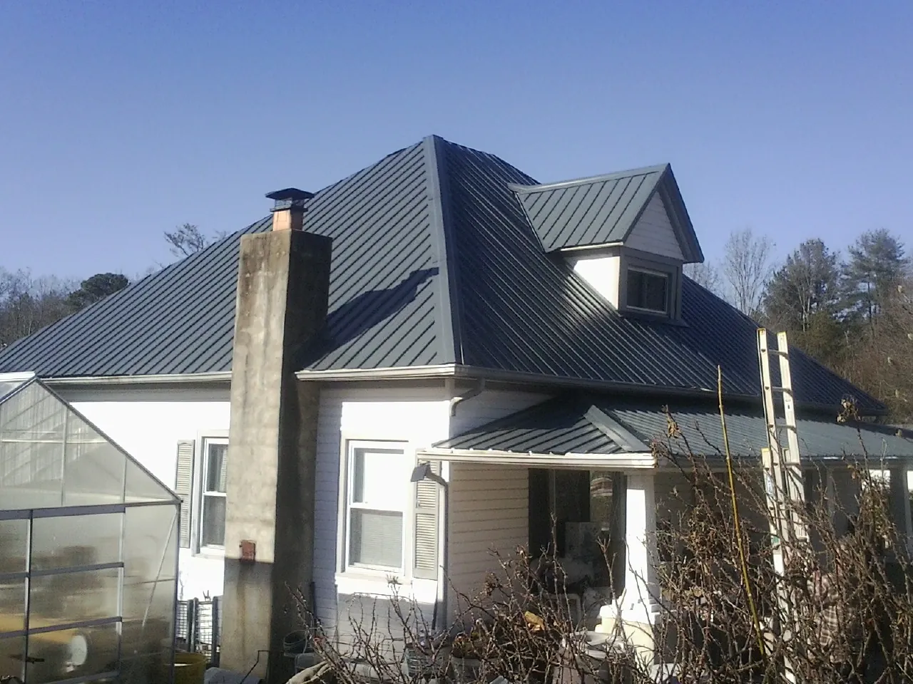 Dark blue standing seam metal roof on a white farmhouse with dormer — Slate & Tile Roof Repair by Roofing Brothers in Rock Springs