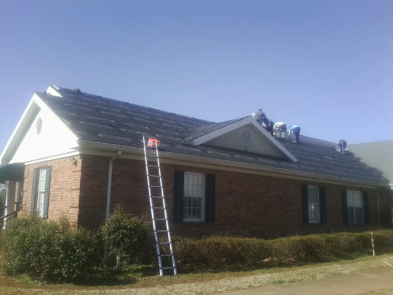 Crew tearing shingles off a brick ranch roof with a ladder set — Emergency Roof Repair work by our crew in Rock Springs