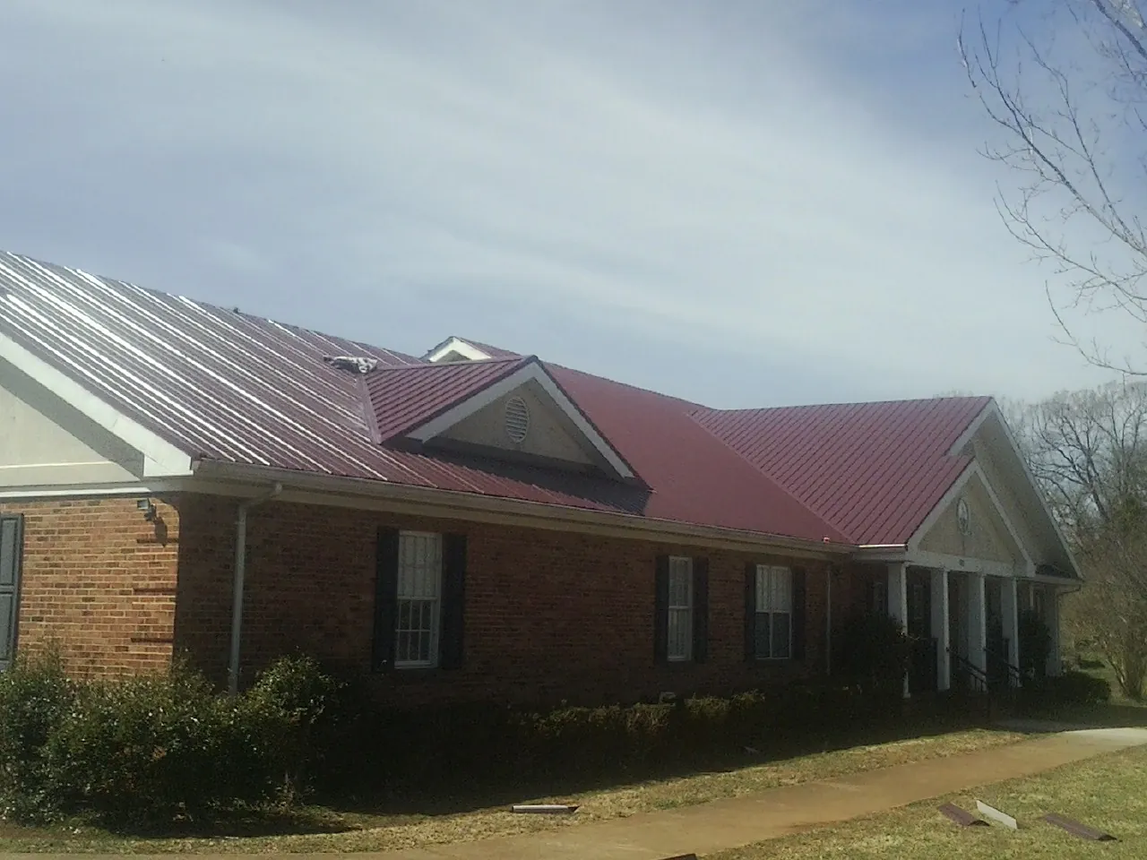 Red metal roof with gabled entries on a long brick building, from a Hail Damage Roof Repair job in Rock Springs