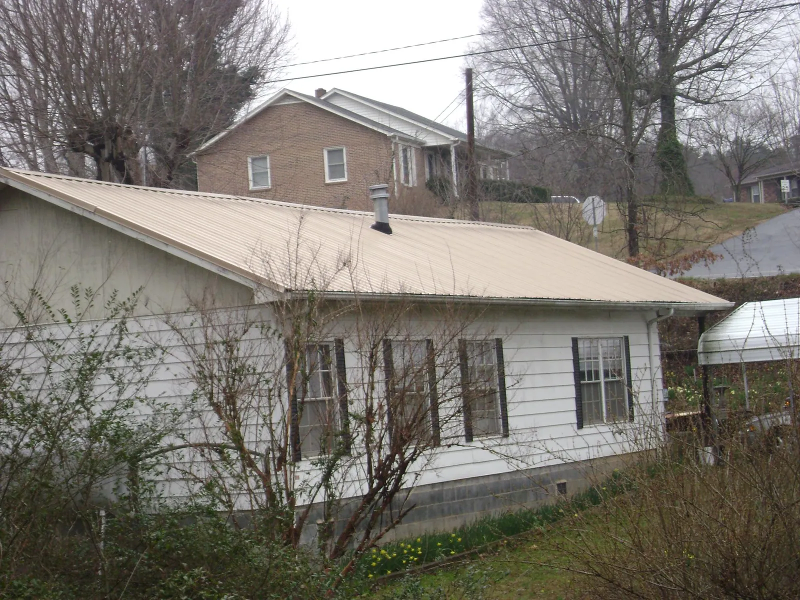 Tan metal roof on a white sided house set into a hillside — Commercial Roofing by Roofing Brothers in Rock Springs